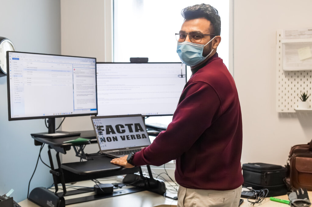 A person in a mask stands at a computer.